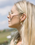 Close-up of a woman with blonde hair wearing gold earrings and sunglasses, outdoors.