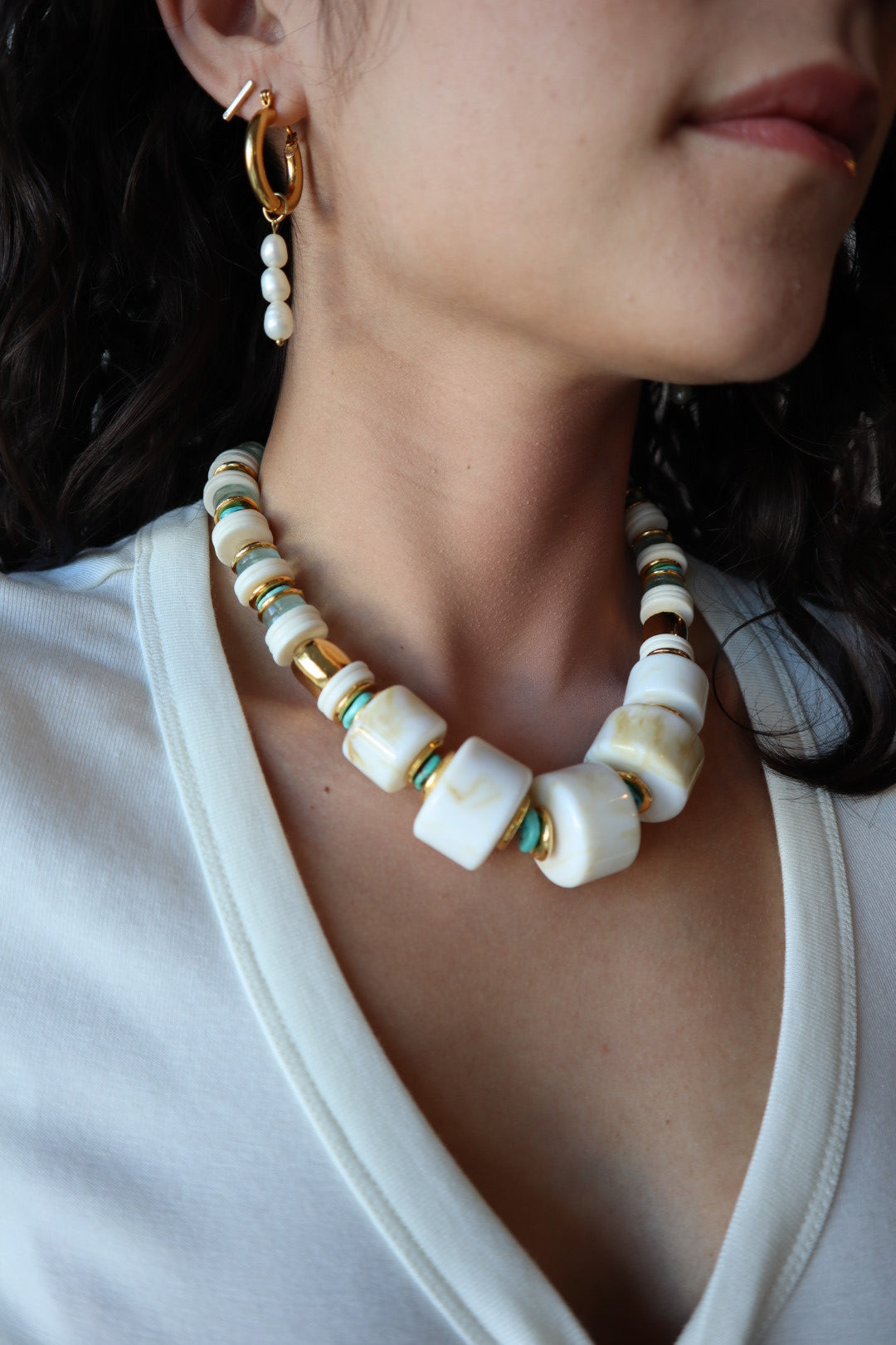 Close-up of a person wearing a beaded necklace with white, gold, and turquoise beads.