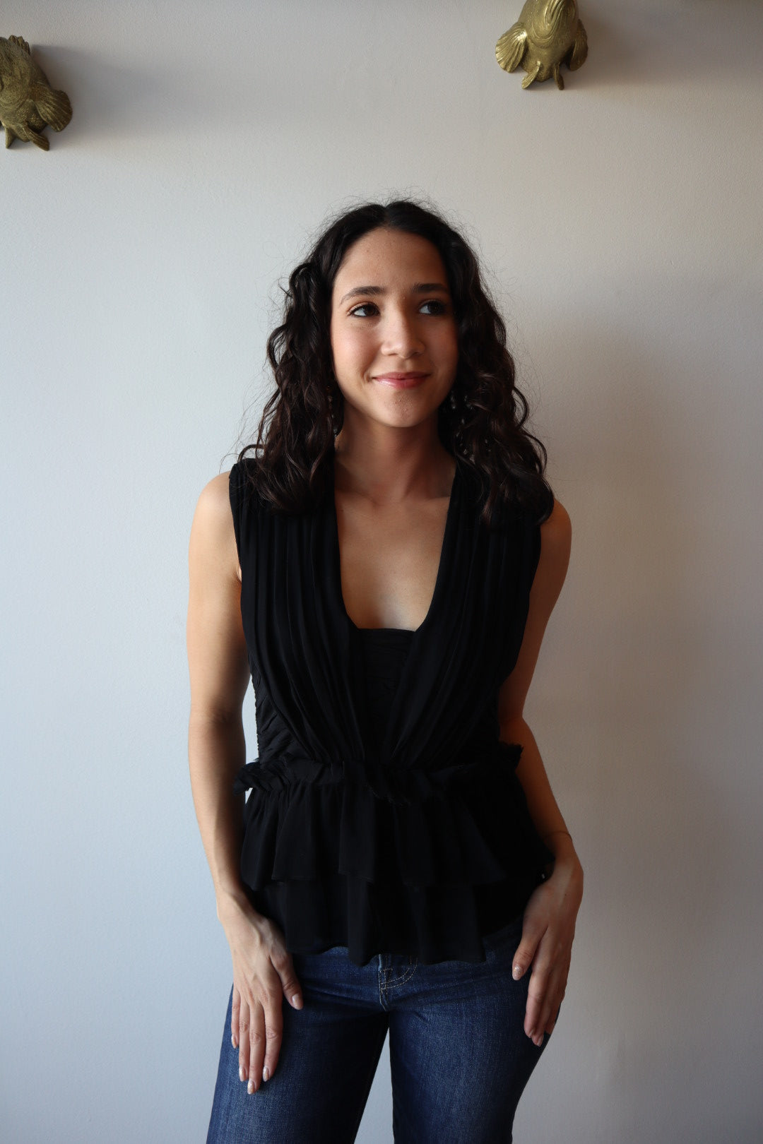 Woman in a black top and blue jeans standing against a plain background