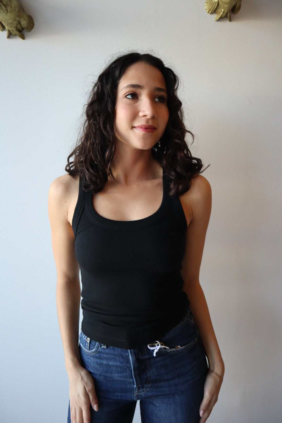 Woman wearing a black tank top and blue jeans against a plain background