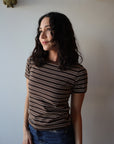 Woman in a striped shirt and jeans standing against a plain wall.