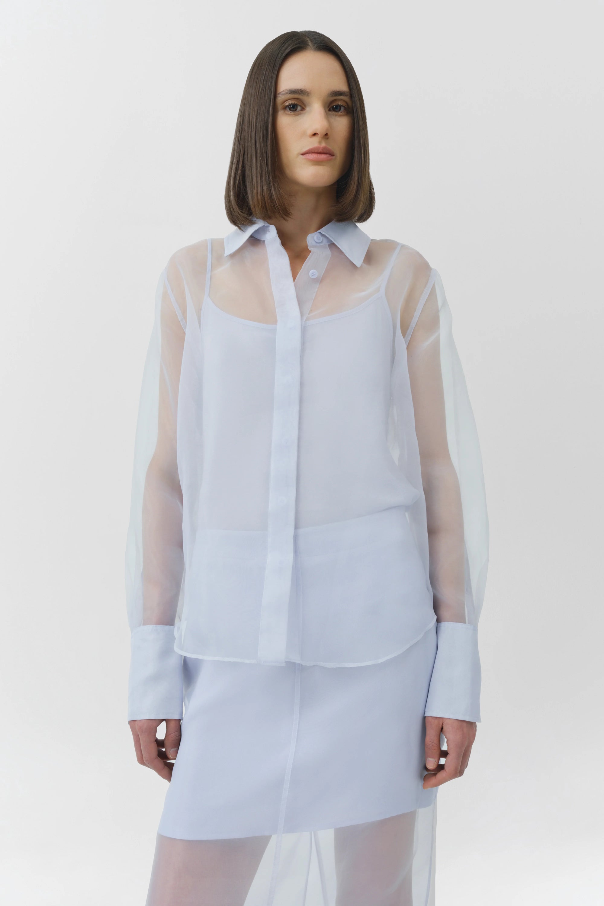 Woman wearing a light blue sheer blouse over a matching skirt on a white background
