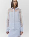 Woman wearing a light blue sheer blouse over a matching skirt on a white background