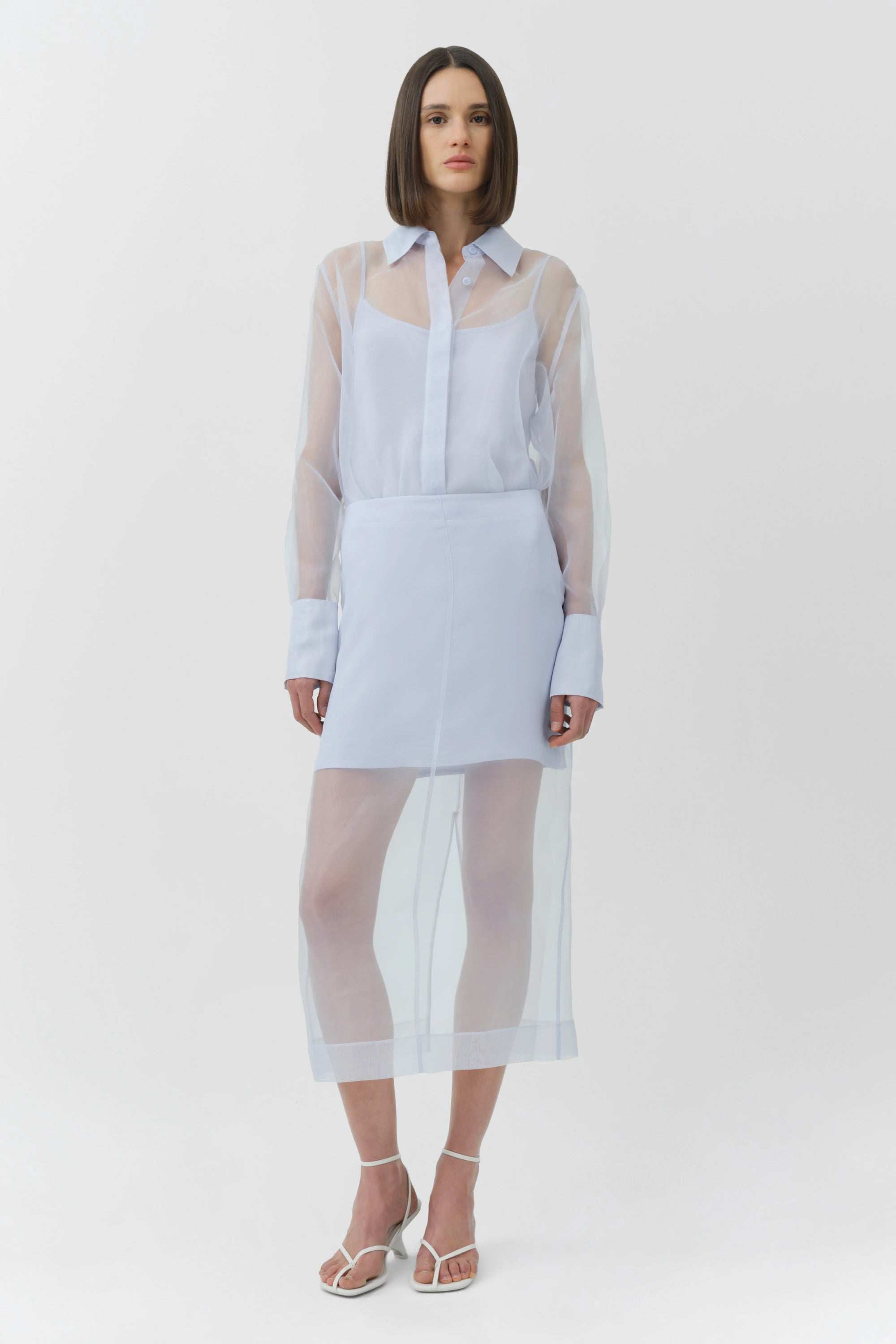 Woman wearing a light blue skirt and top with sheer sleeves on a white background