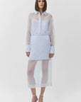 Woman wearing a light blue skirt and top with sheer sleeves on a white background