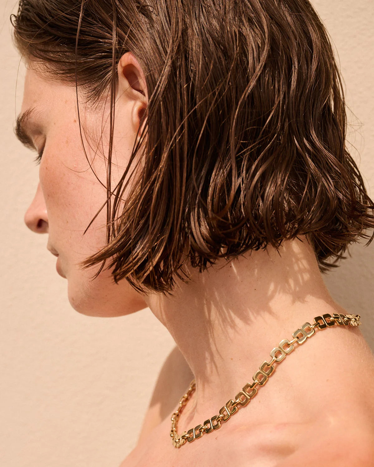 Close-up of a person wearing a gold chain necklace against a beige background