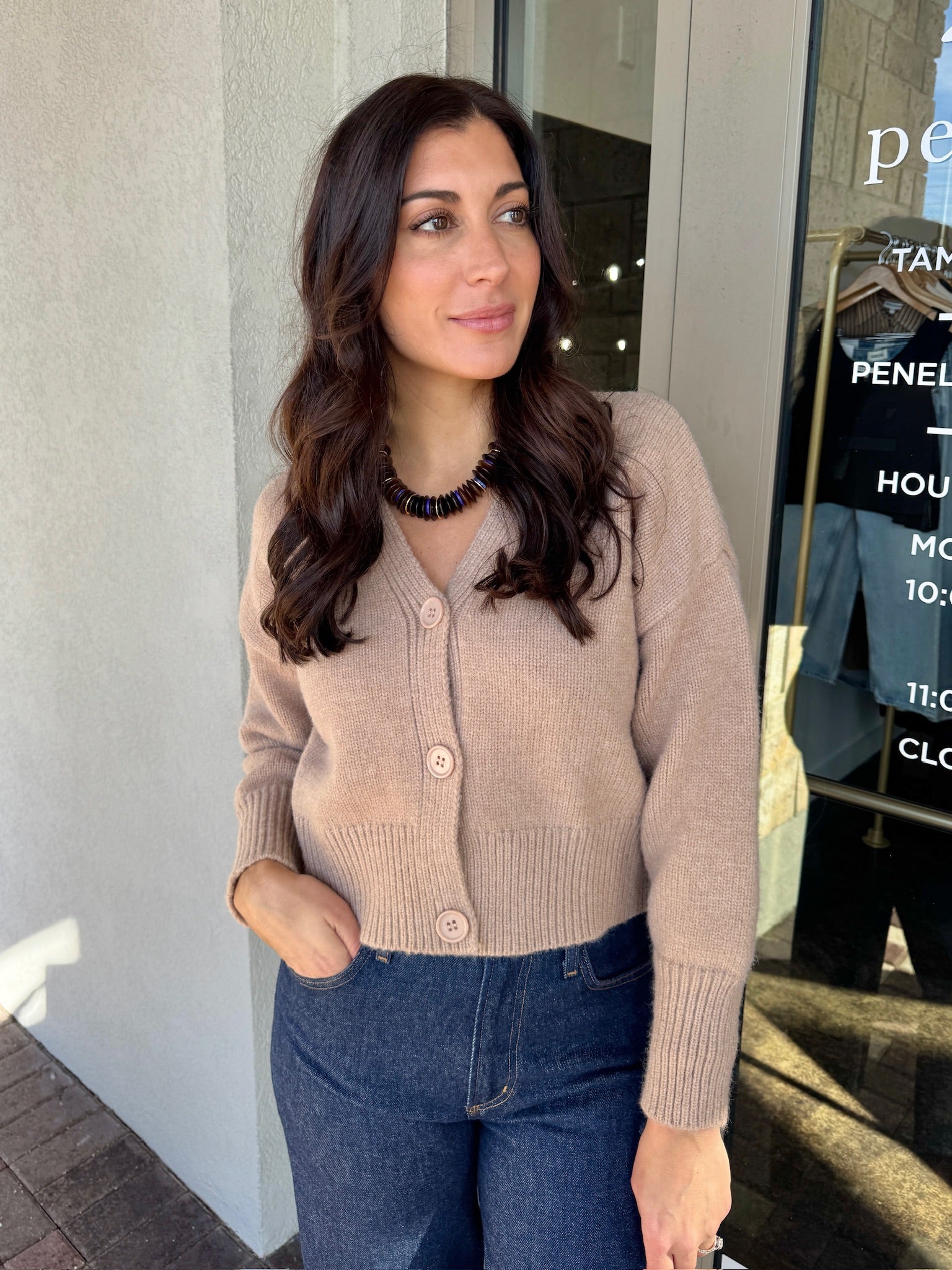 Woman wearing a beige cardigan and blue jeans standing outside a store.