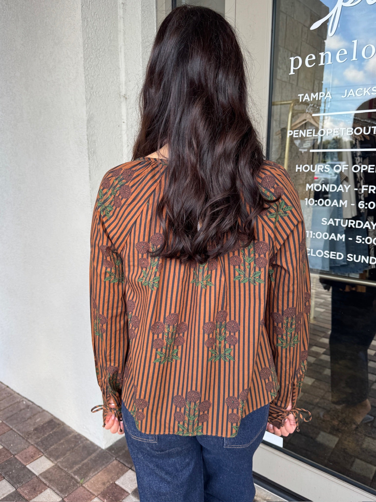 Person wearing a patterned shirt standing in front of a store entrance, back