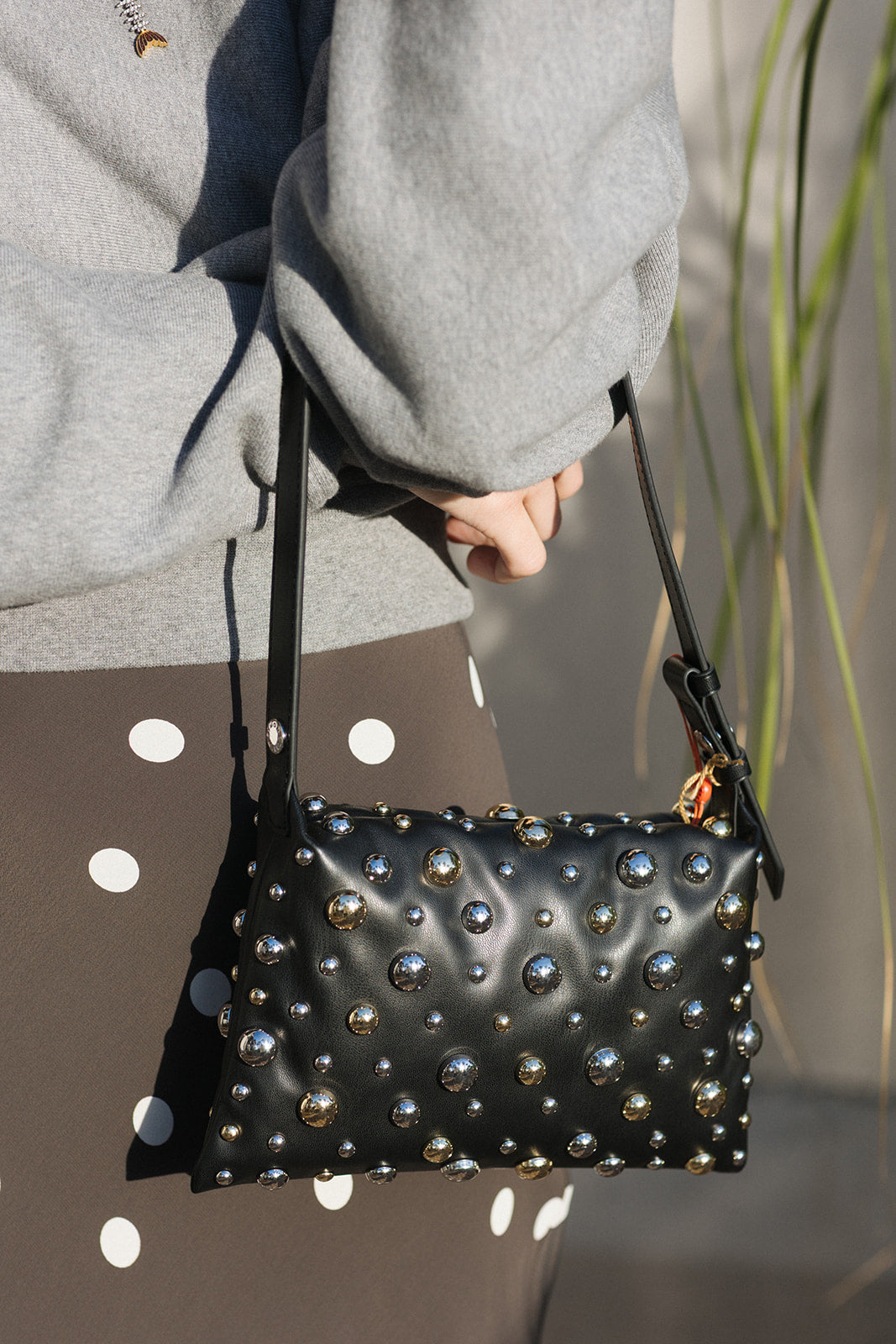 Black studded handbag held by a person wearing a gray sweater.