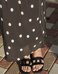 Person wearing a black dress with white polka dots and black sandals on a stone pavement.