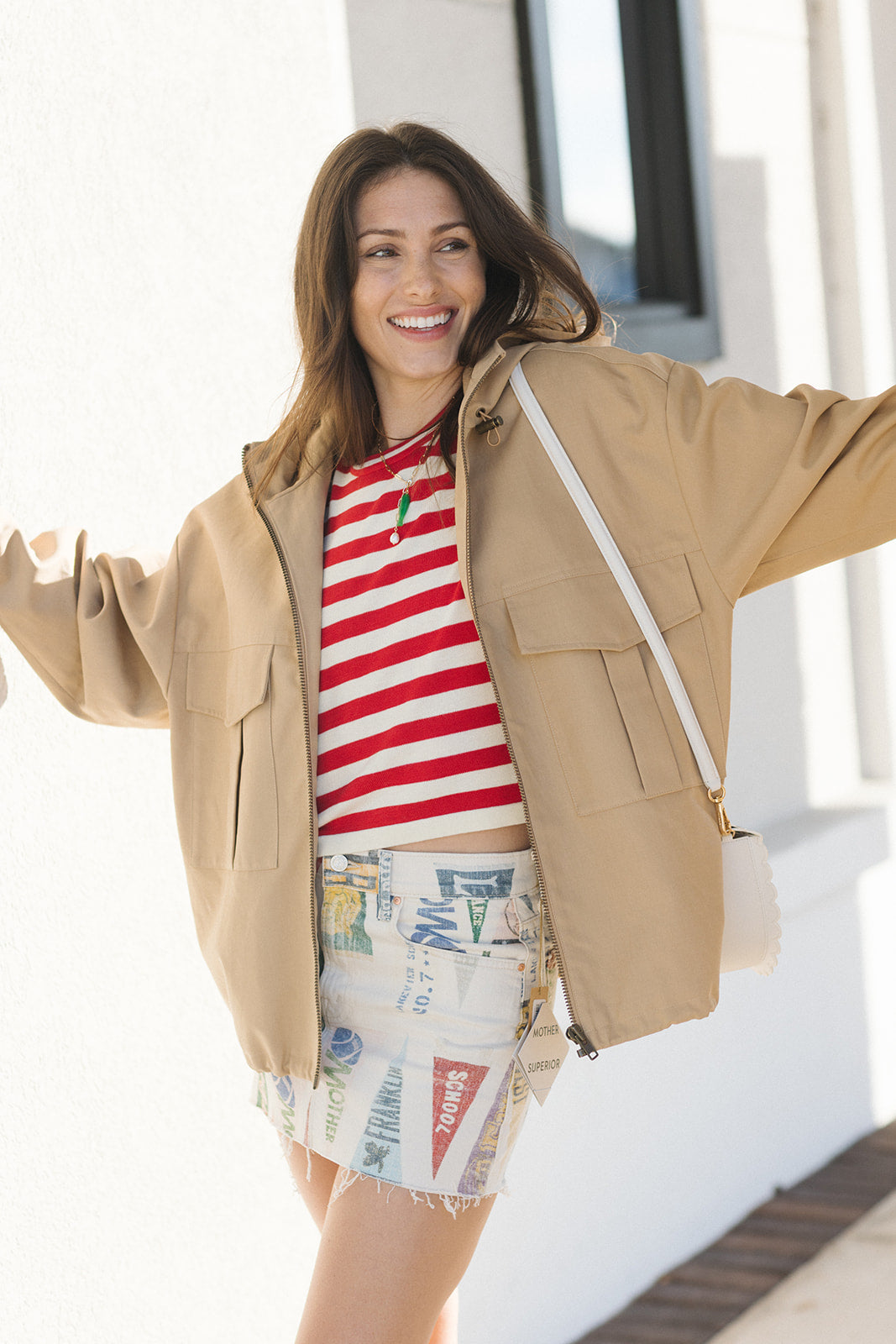 Woman wearing a beige jacket, red and white striped shirt, and patterned skirt outdoors.