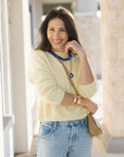 Woman wearing a light yellow sweater and blue jeans, standing outdoors.