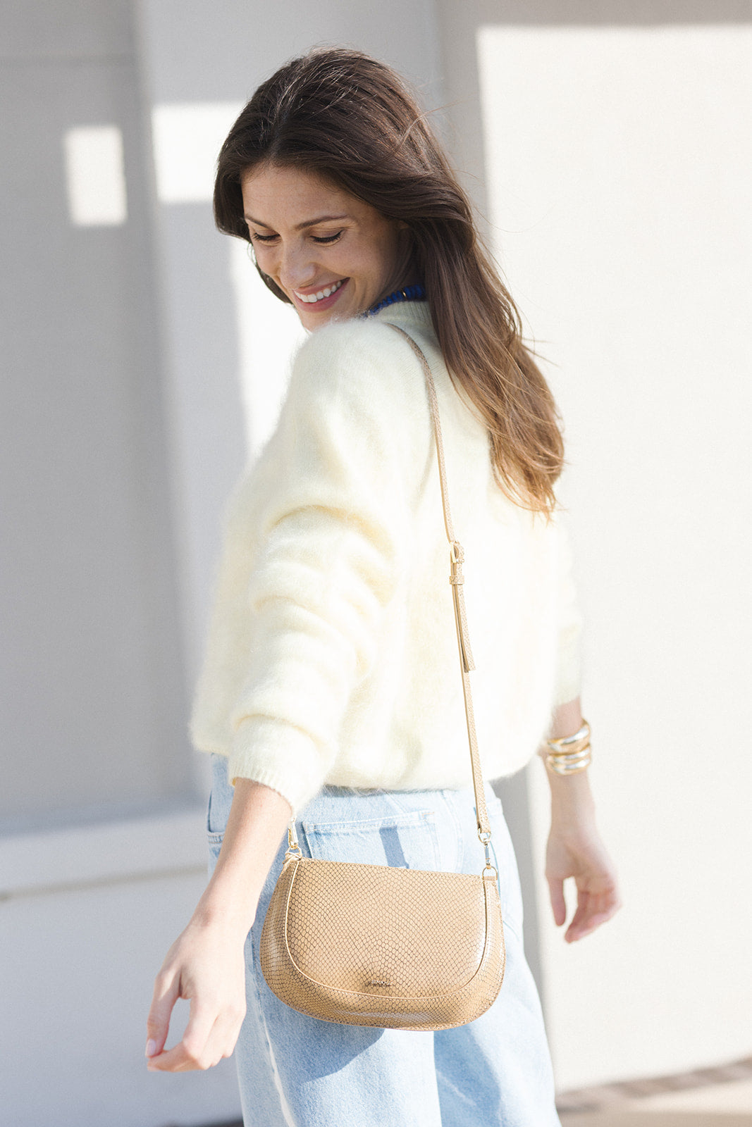 Woman wearing a light-colored sweater and carrying a beige handbag indoors.