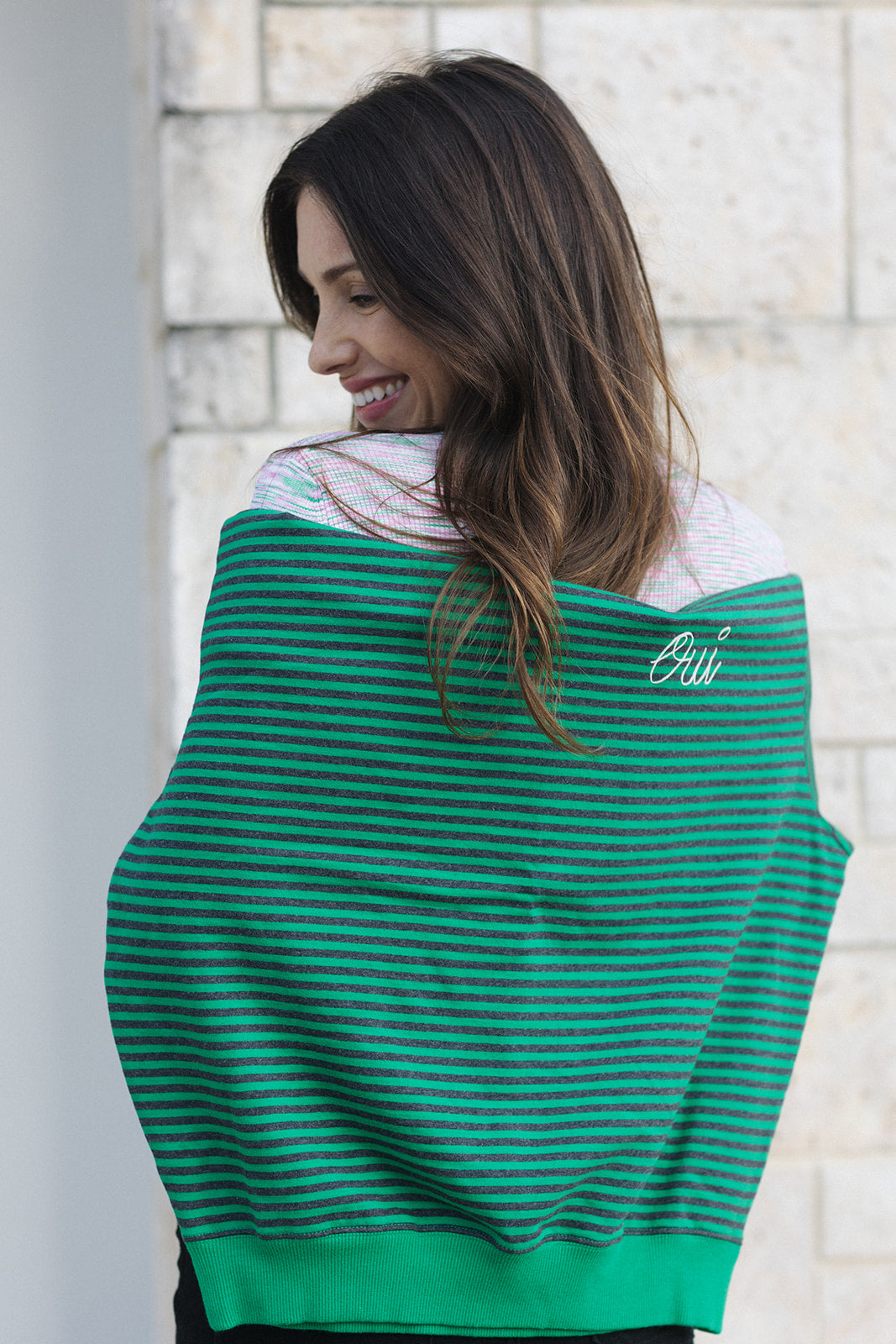 Woman wearing a green striped sweater with 'Citi' logo against a light stone wall.