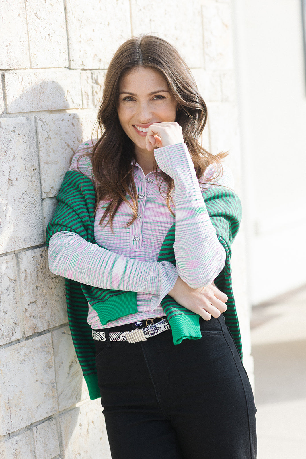 Woman wearing a green cardigan over a striped shirt against a stone wall.