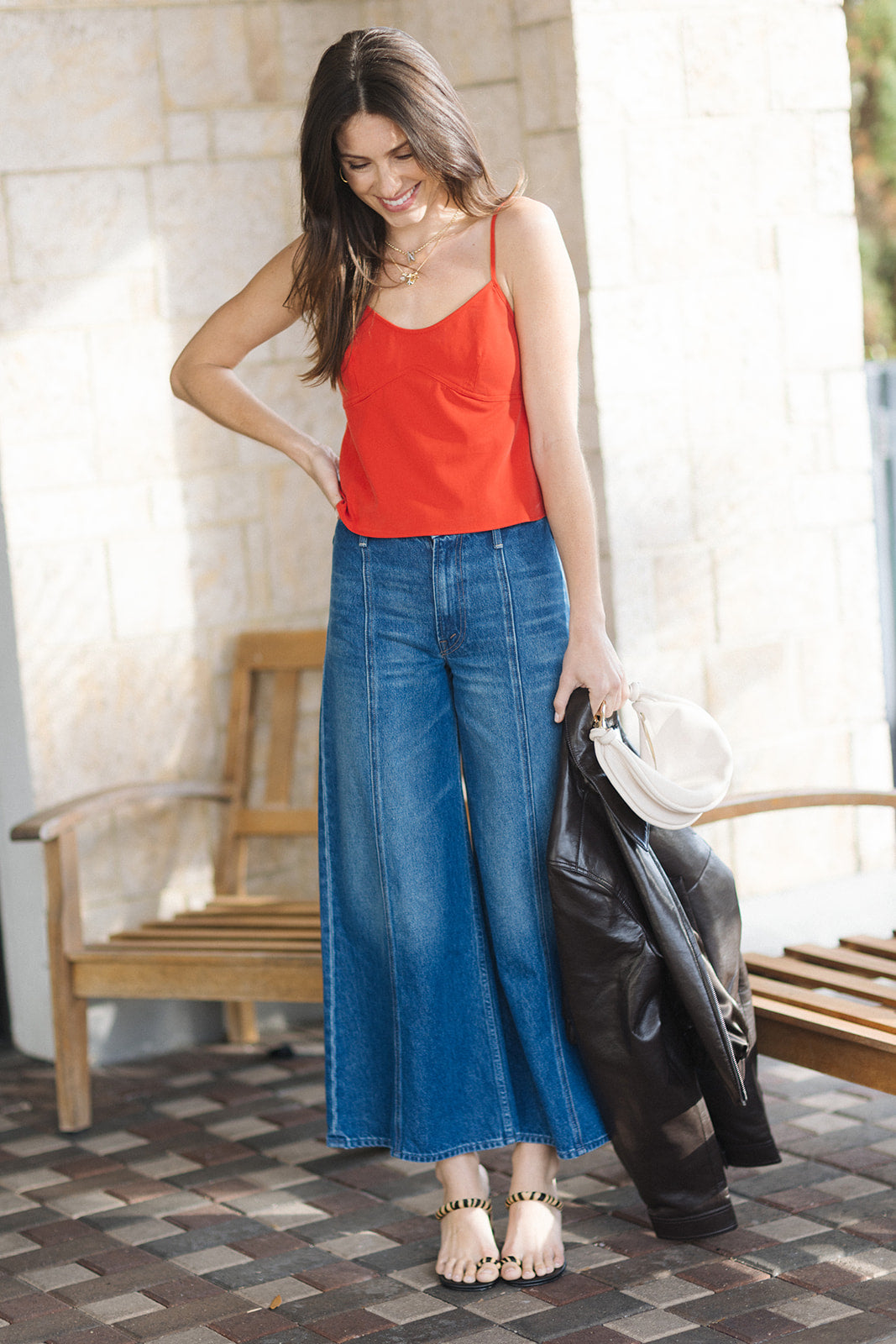 Woman wearing a red top and blue jeans standing outdoors.