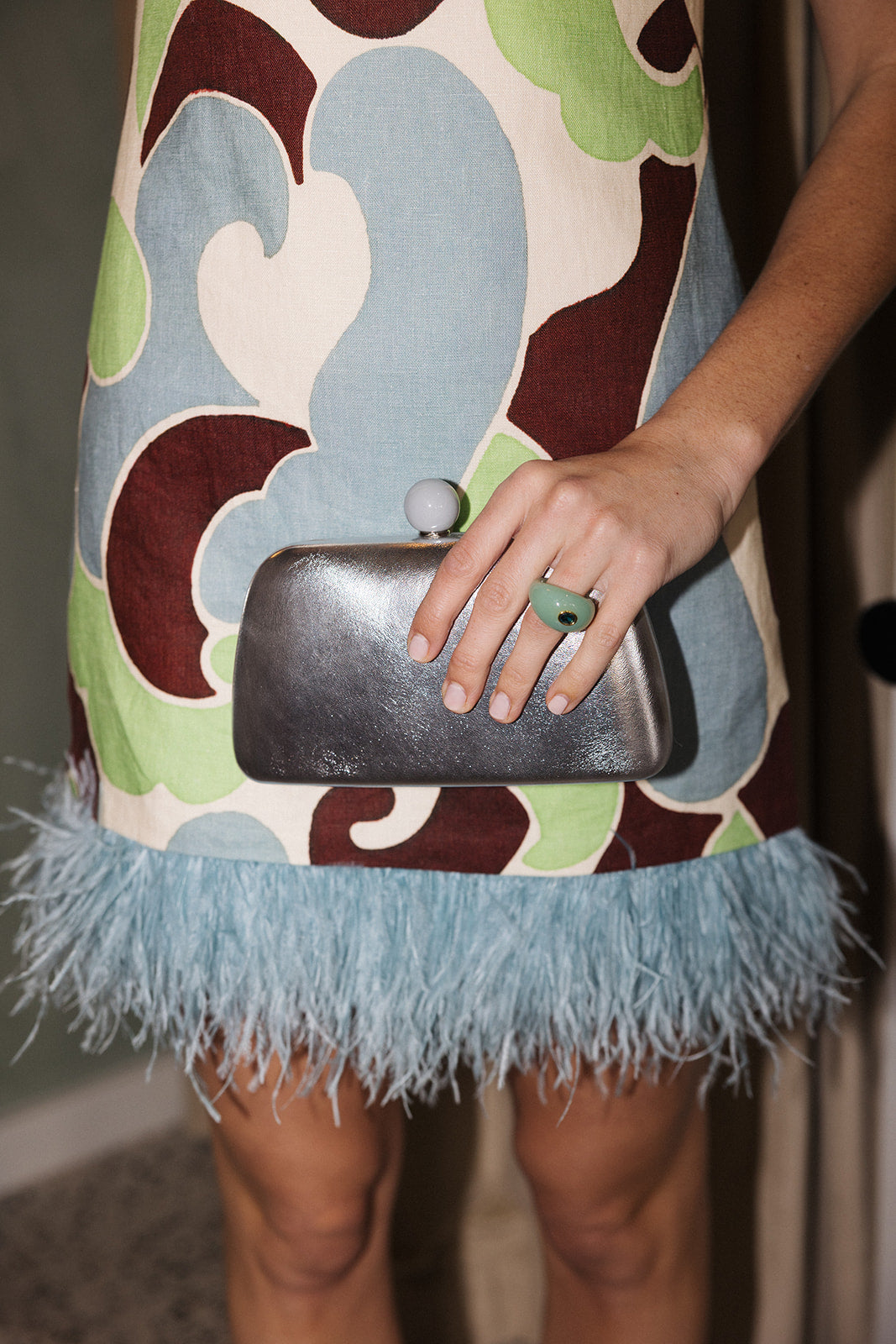 Person wearing a colorful dress with feathered hem and holding a silver clutch.