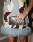 Person wearing a colorful dress with feathered hem and holding a silver clutch.