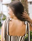A woman shown from behind wearing a brown and cream striped crop top with tie straps and a gold zipper at the back, photographed outdoors.