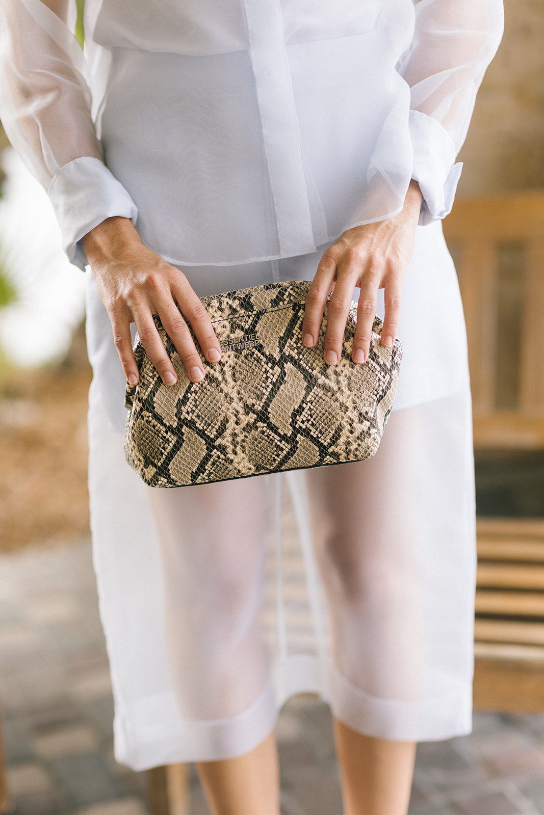 A person heolding a rectangular clutch bag with a beige and black snakeskin pattern.