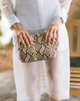 A person heolding a rectangular clutch bag with a beige and black snakeskin pattern.
