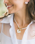 A close-up lifestyle shot of a woman wearing a pearl with gold heart pendant and a white collared shirt.