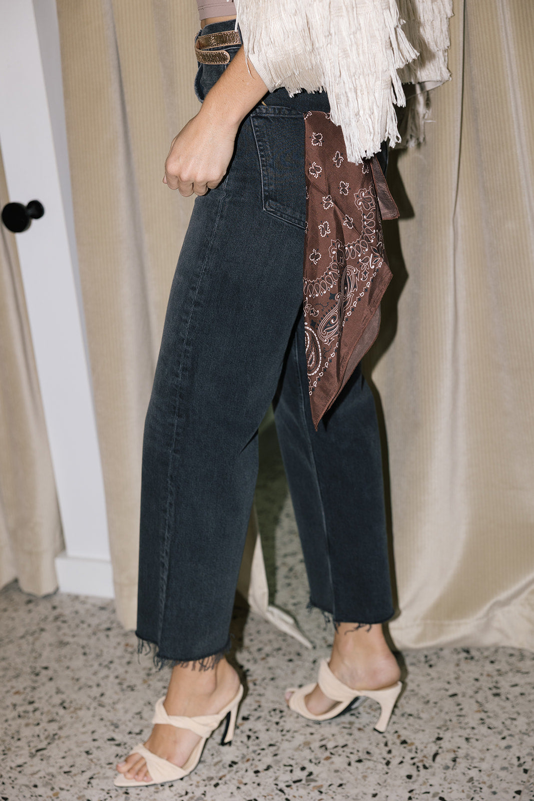 The silky bandana in the pocket of black jeans on a model with heels and a fringe cardigan 