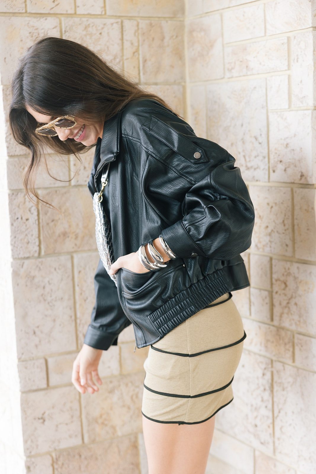 Early oversized faux leather coat on a model with a silver bag and mini dress wearing sunglasses, side