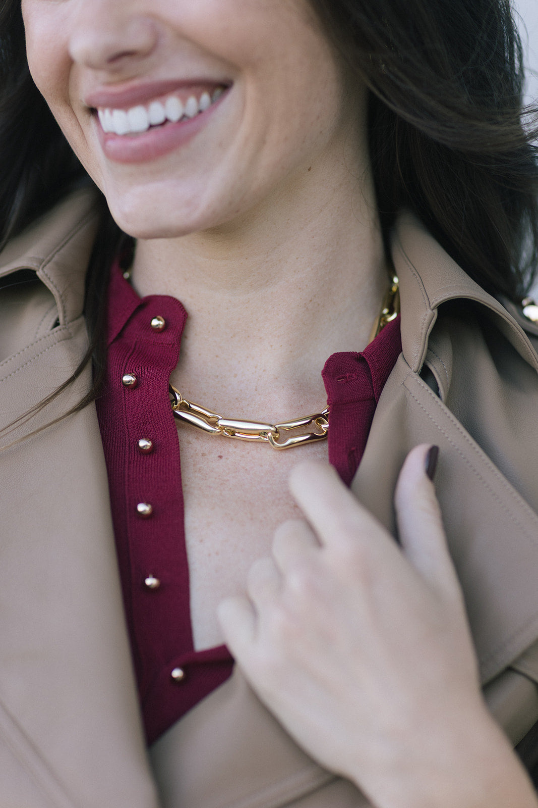model wearing a gold link necklace with a wine colored top and tan jacket over top 