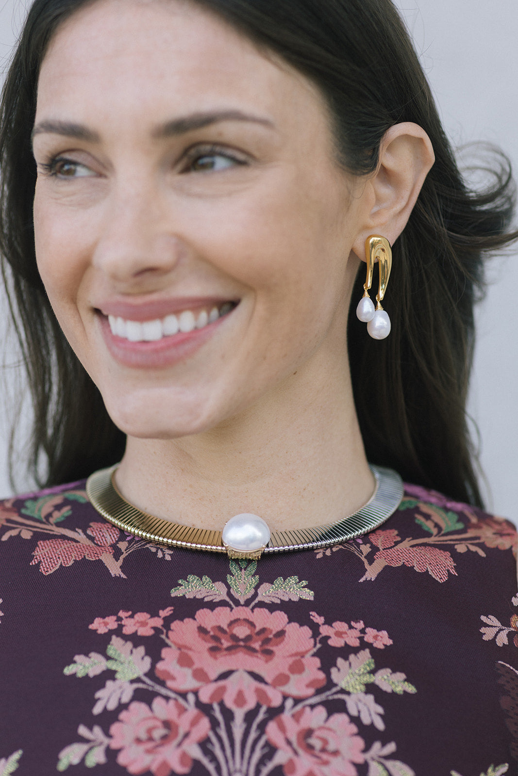 model wearing a floral top with a two tone necklace with a large pearl at the center with gold earrings that have a double pearl drop 