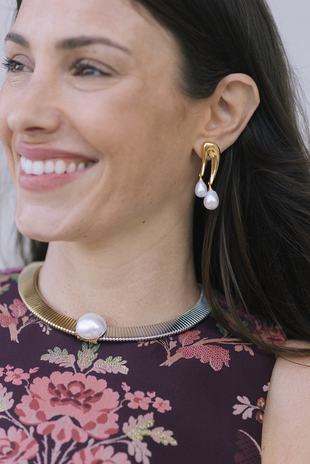 model wearing a floral top with a two tone necklace with a large pearl at the center with gold earrings that have a double pearl drop 