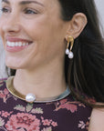 model wearing a floral top with a two tone necklace with a large pearl at the center with gold earrings that have a double pearl drop 
