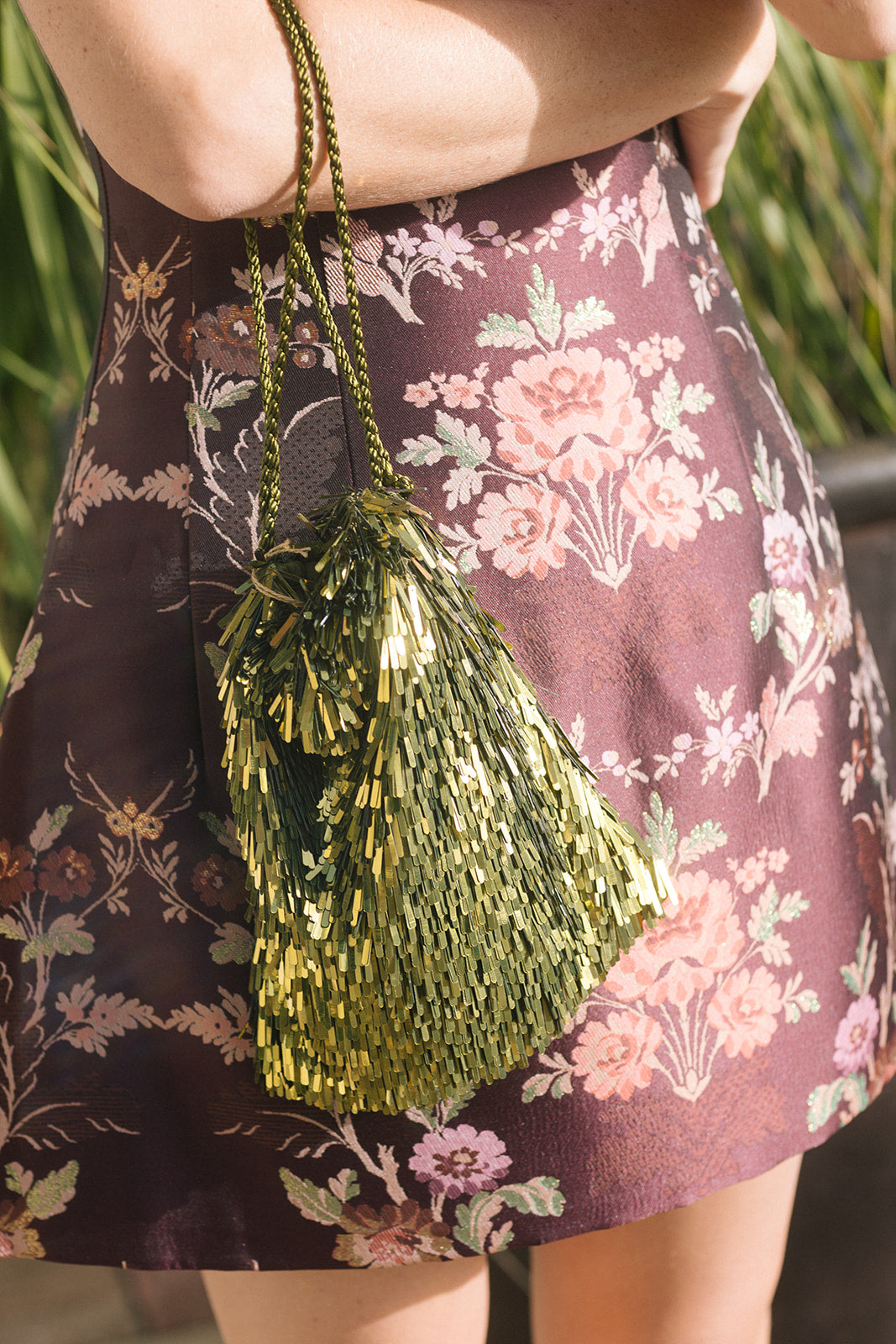 model holding a green fringe bag against a wine colored floral print mini dress 