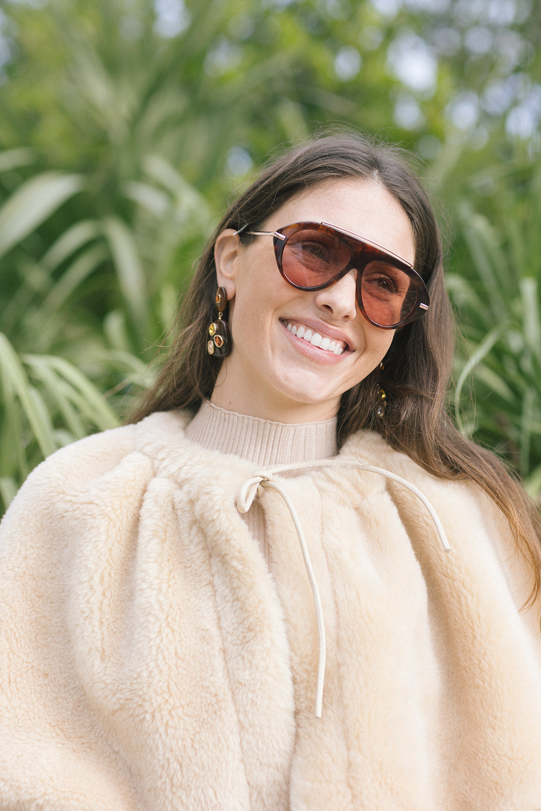 model wearing tortoise sunglasses and a tan fur cape that ties at the neck, close up 
