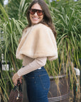 model wearing a tan fur cape over a long sleeve top with dark blue jeans outside, side view