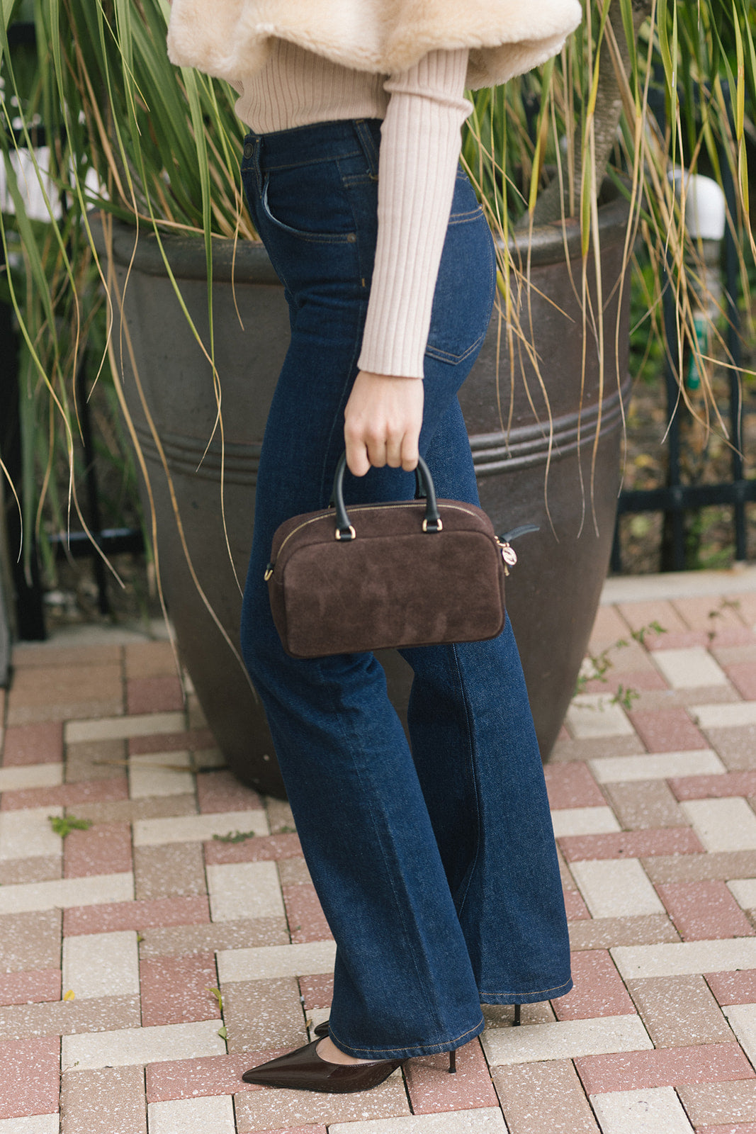 model holding a small rectangle suede brown bag by her side against dark jeans