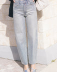 model wearing light blue jeans covered in rhinestones and a white top with a dark jacket over holding a purse 