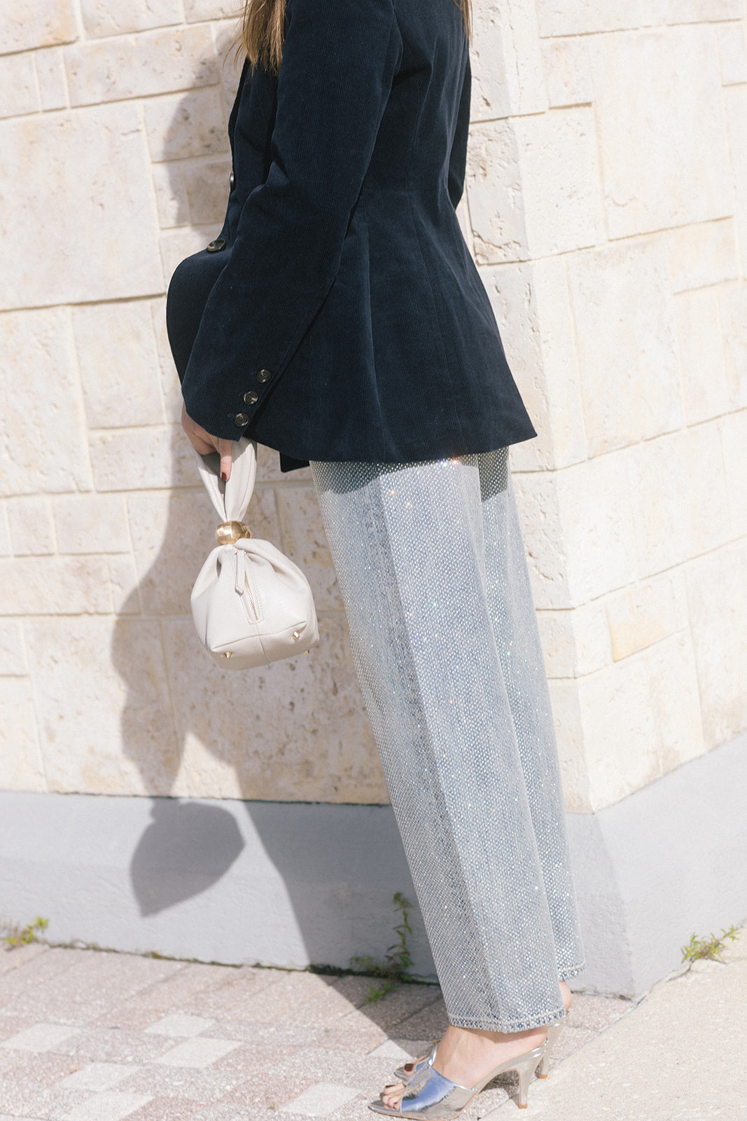 model wearing light blue jeans covered in rhinestones and a dark blazer holding a purse, side view
