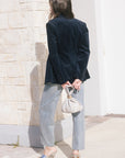 model wearing a navy blazer withe rhinestone jeans holding a cream bag, outside, back view