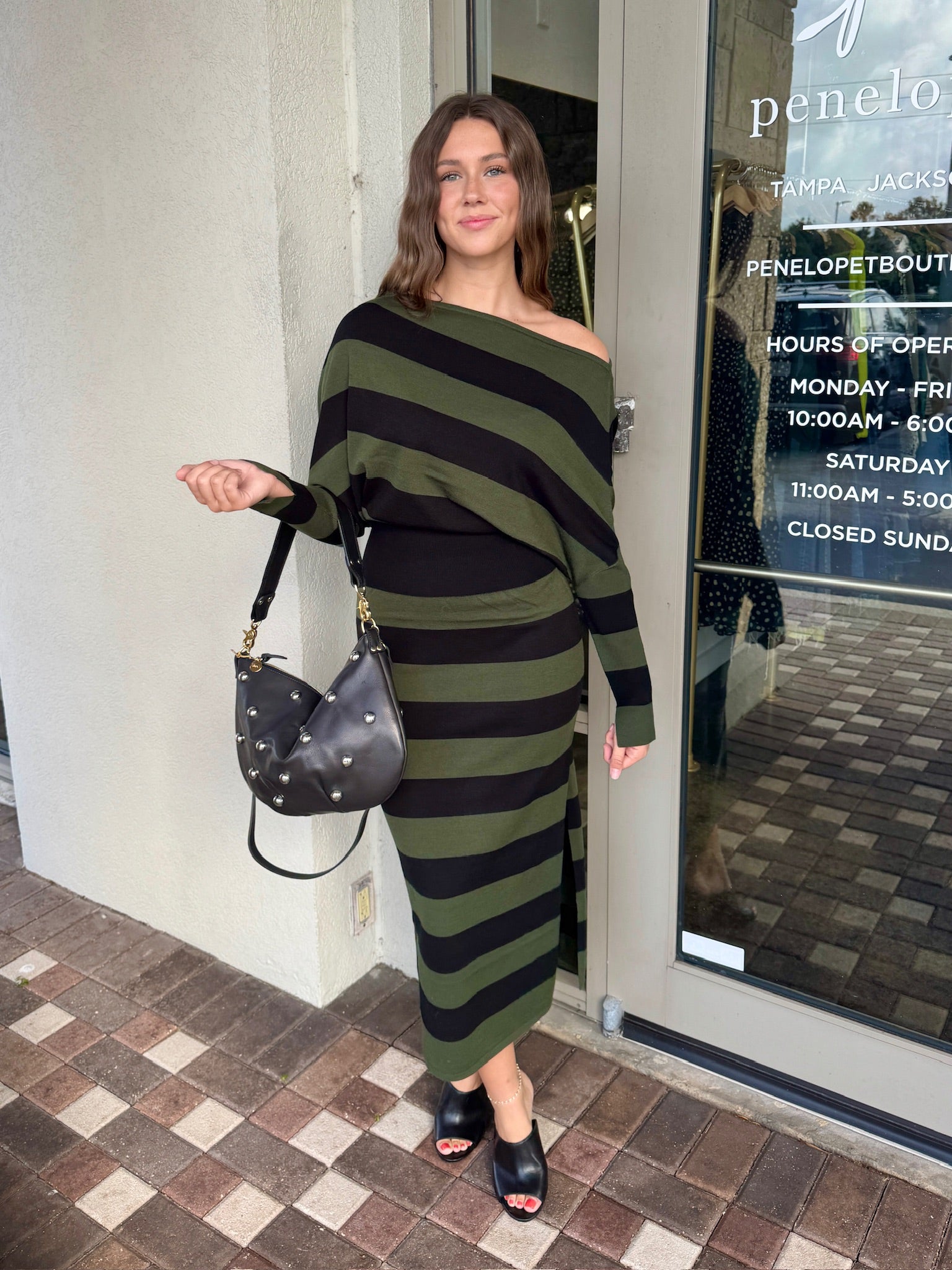Woman in a green and black striped dress standing outside a store.