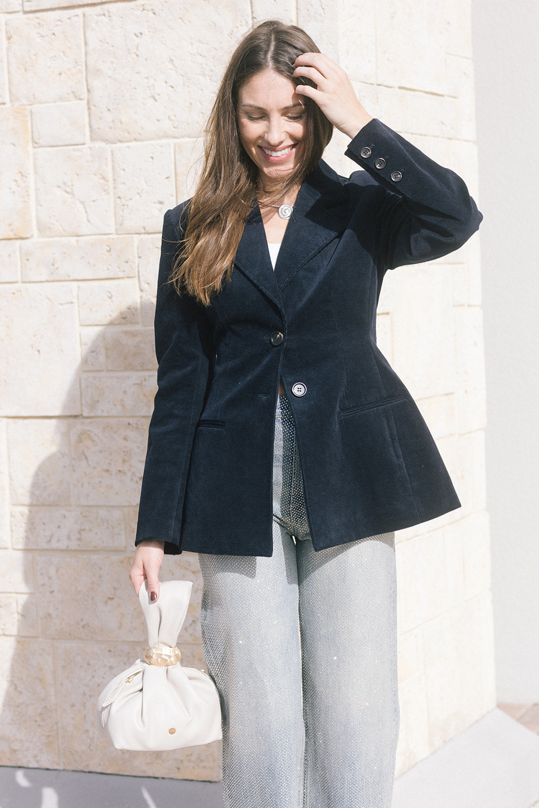 model wearing a navy blazer withe rhinestone jeans holding a cream bag, outside