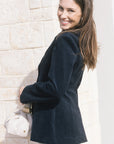 model wearing a navy blazer withe rhinestone jeans holding a cream bag, outside, side view