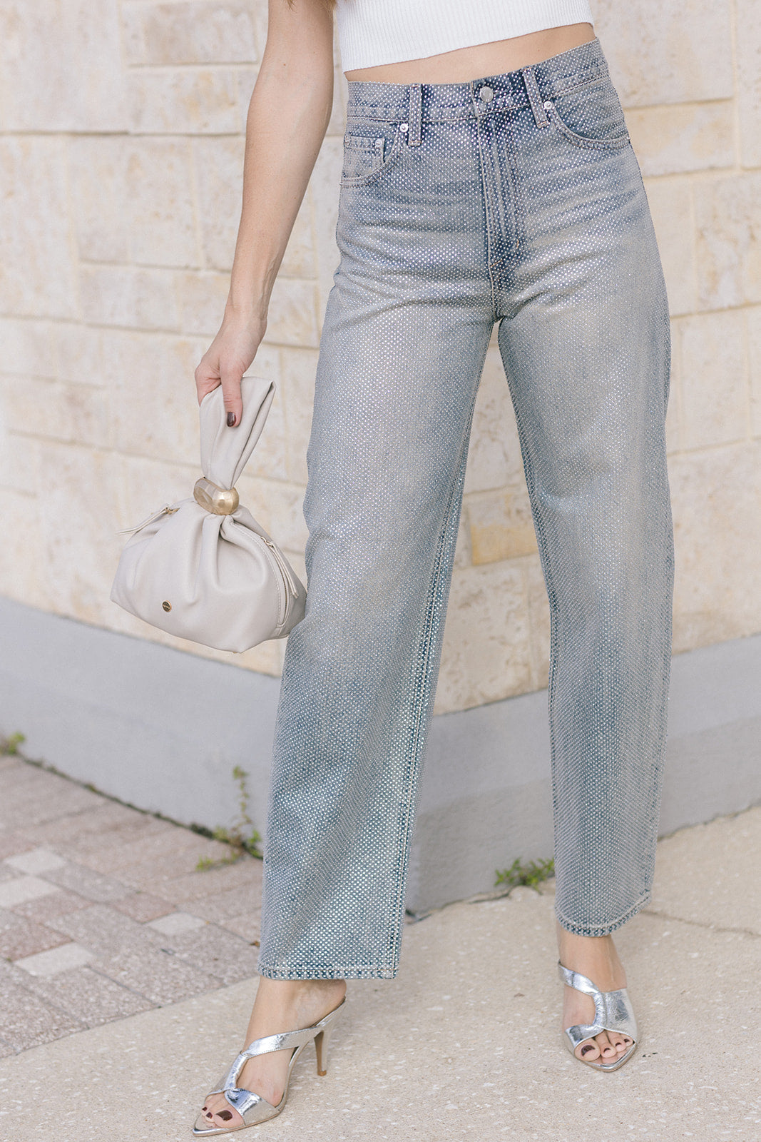 model wearing light blue jeans covered in rhinestones and a white top holding a purse 