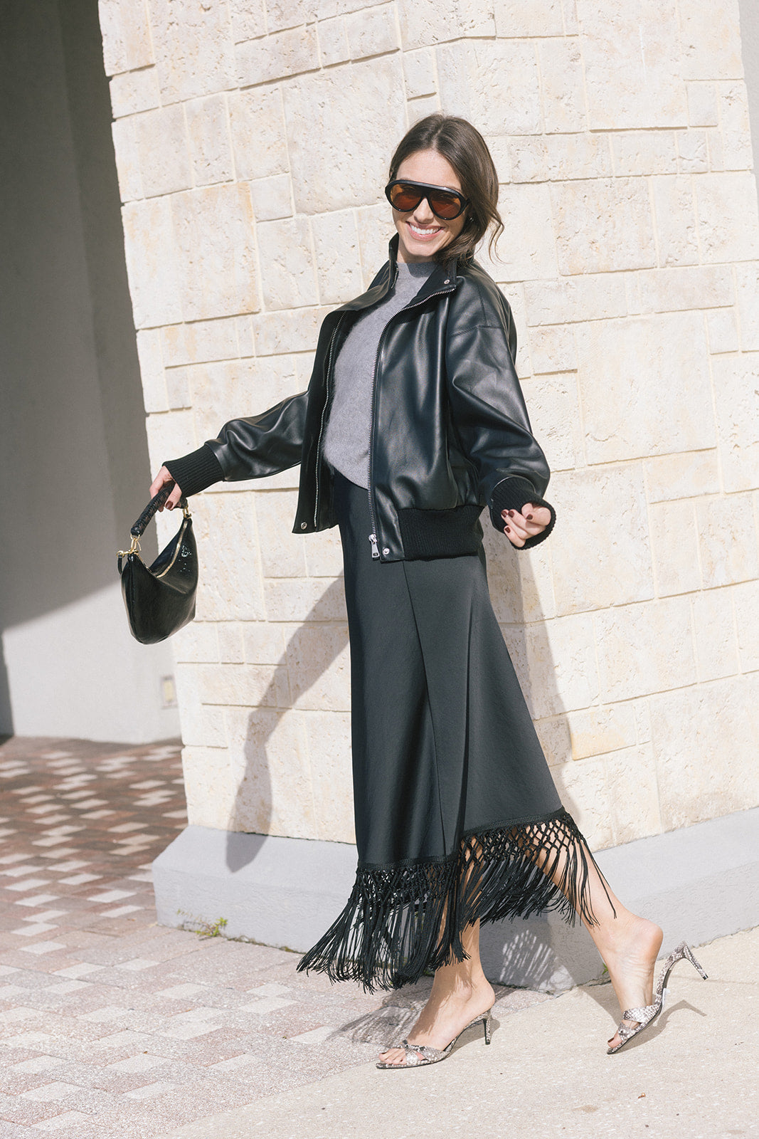 model wearing a black jacket with a grey top paired with a black skirt with fringe at the bottom 