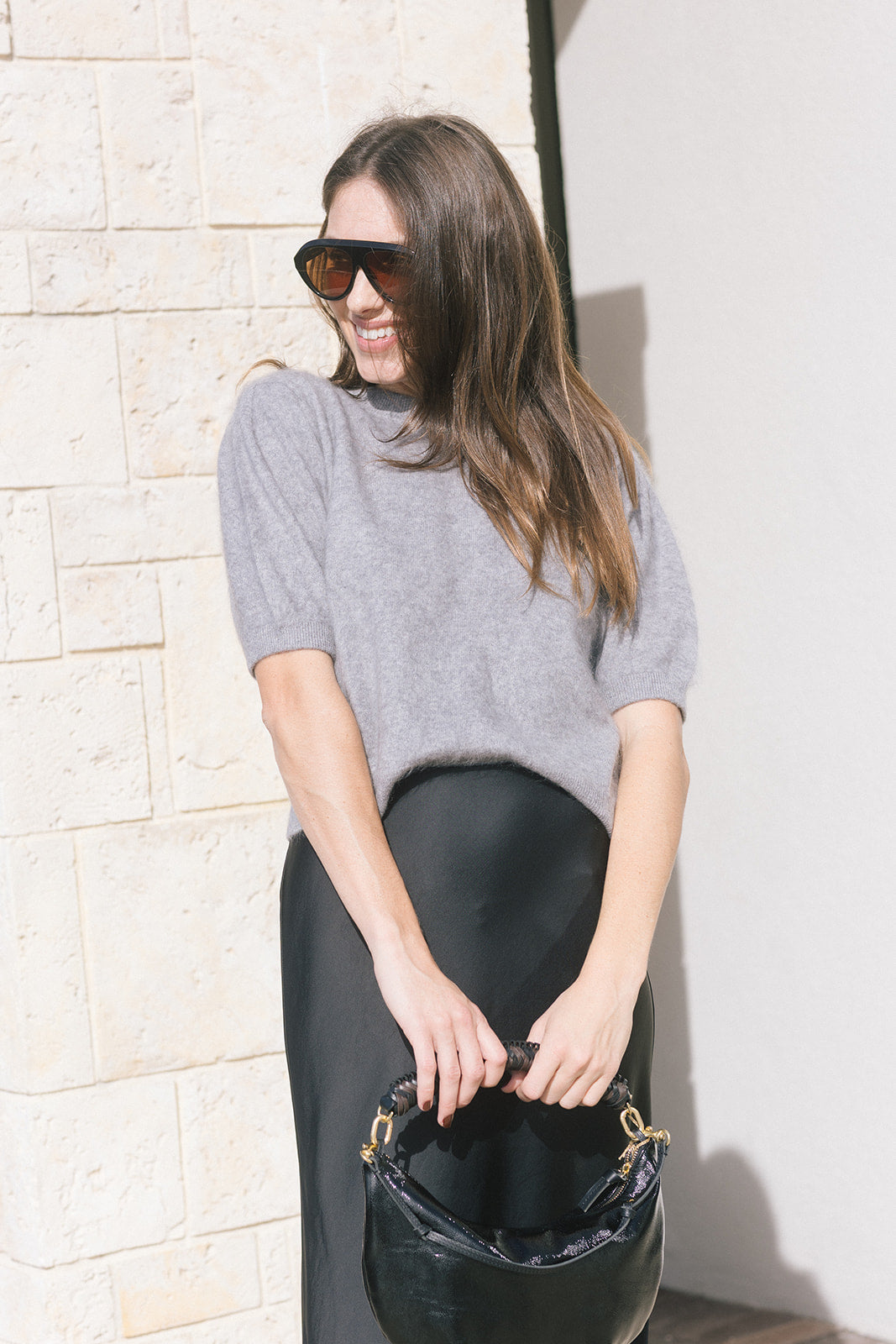 model wearing a grey short sleeve sweater and a black skirt holding a black bag