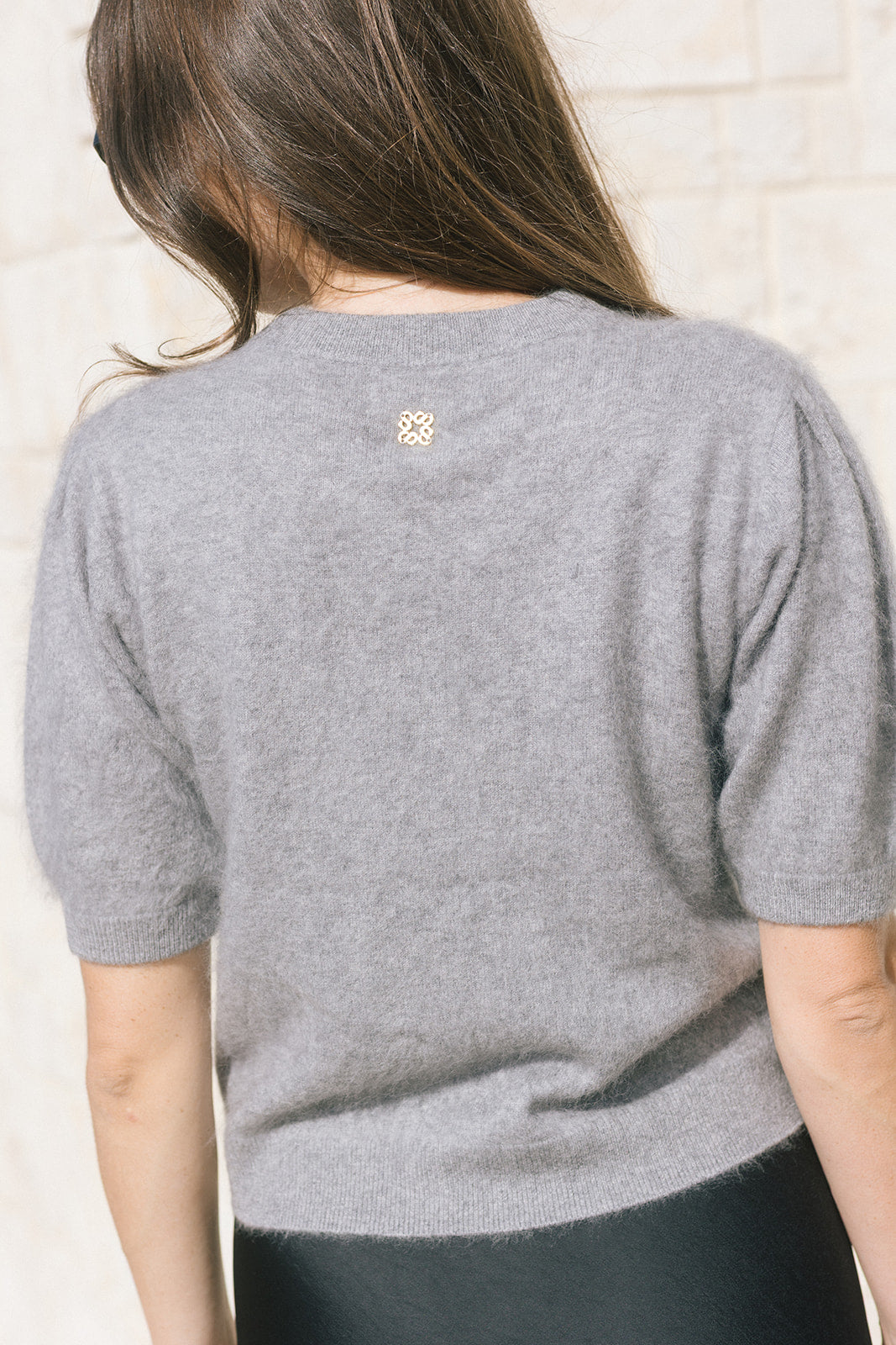 model wearing a grey short sleeve sweater and a black bottom, pictured from behind 