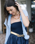 Woman wearing By the Sea Necklace in Terracotta, a blue cardigan over a dark dress with a gold belt, indoors.
