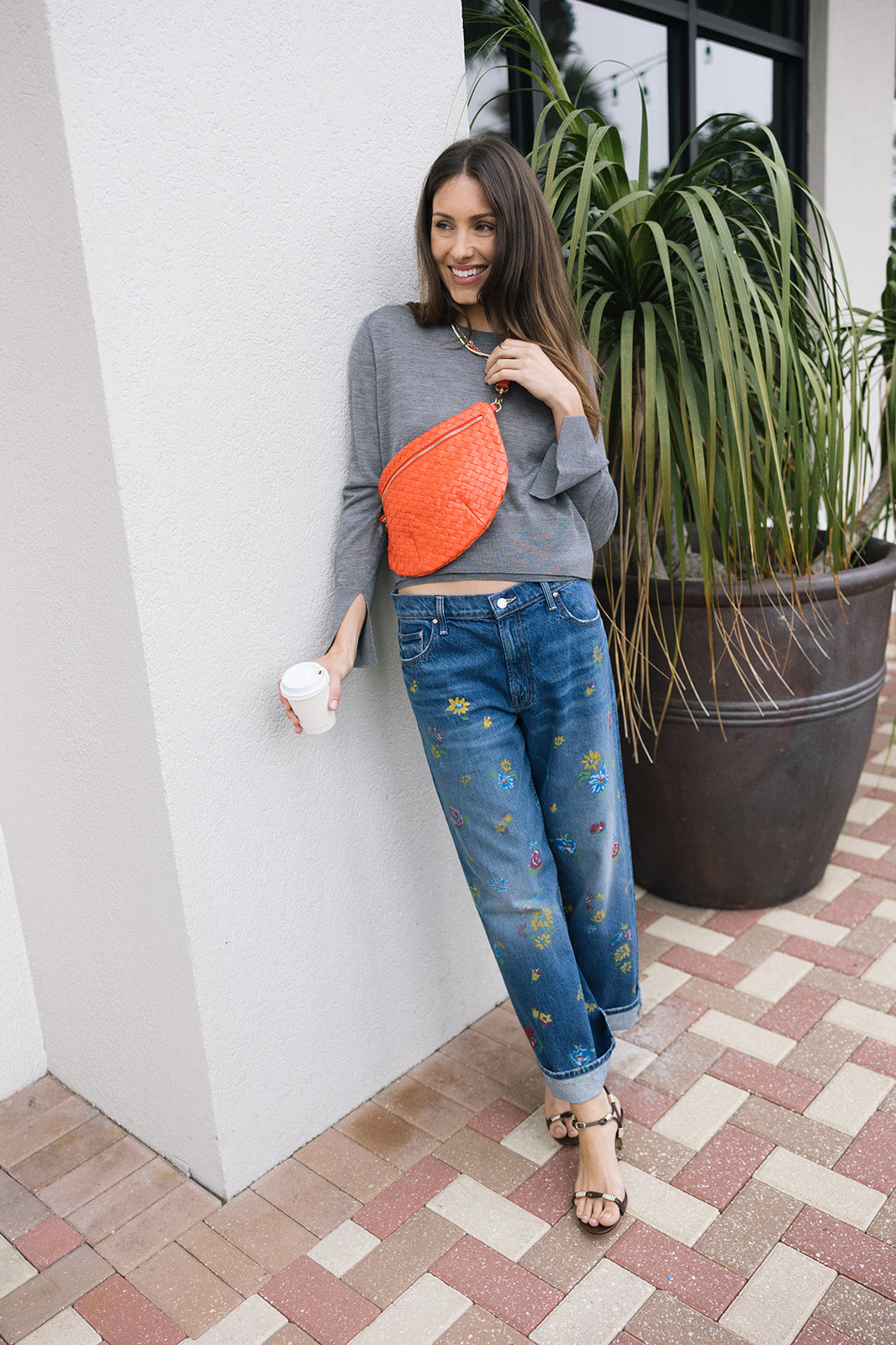 Woman wearing a gray sweater  and The Lil Rerun Zip Sneak, standing next to a plant.