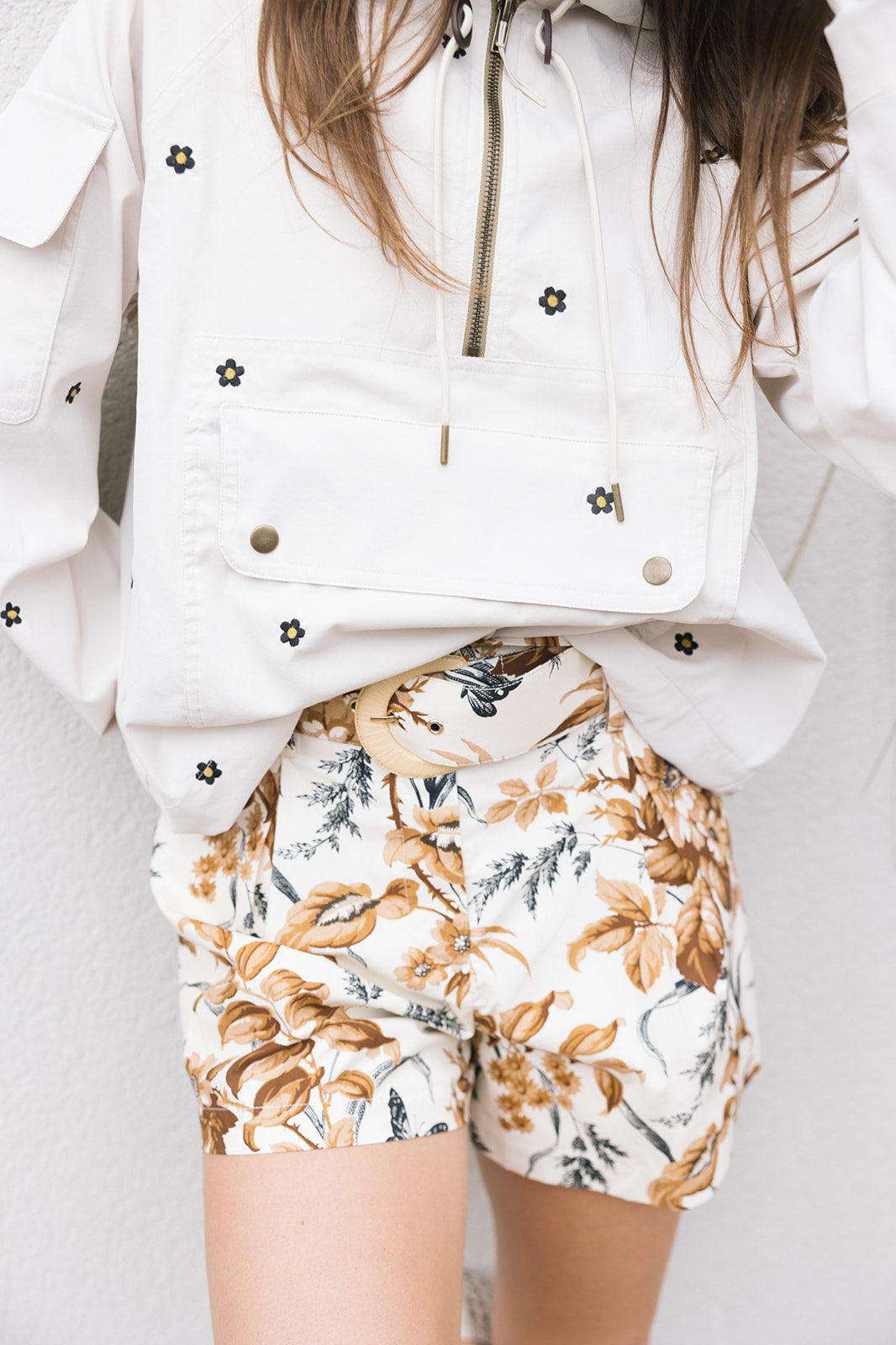 Person wearing a white jacket with floral patterns and floral shorts on a light background