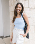 Woman in light blue top and white shorts standing against a stone wall.